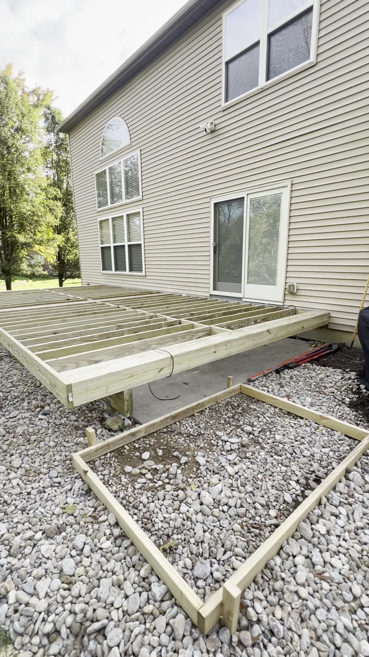 Treated timber deck frame laid out over a gravel bed at the back of a tan sided home before the composite boards go down