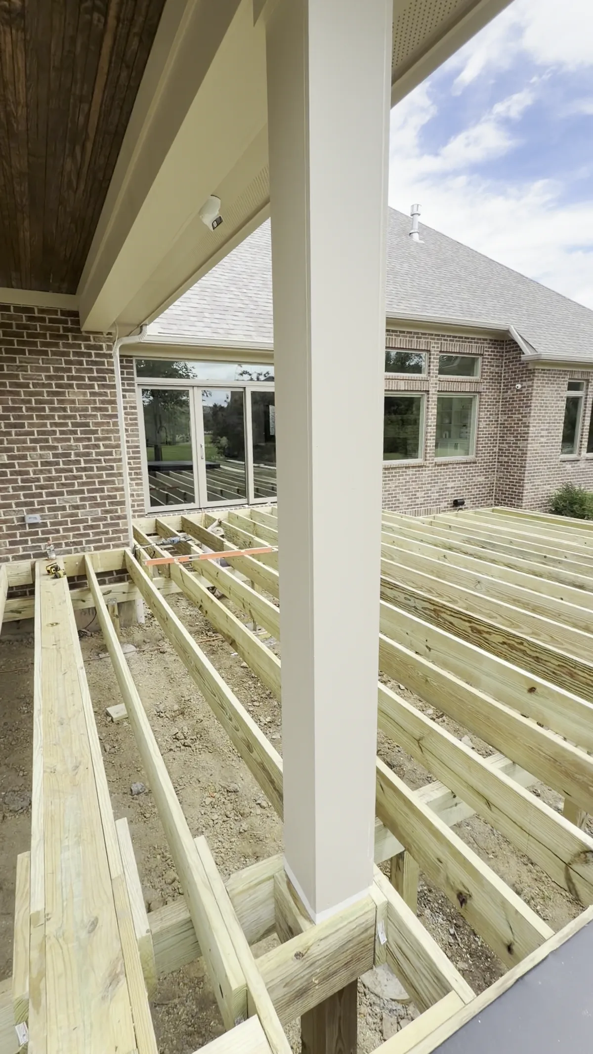 Deck frame under construction beneath a covered porch at a brick home