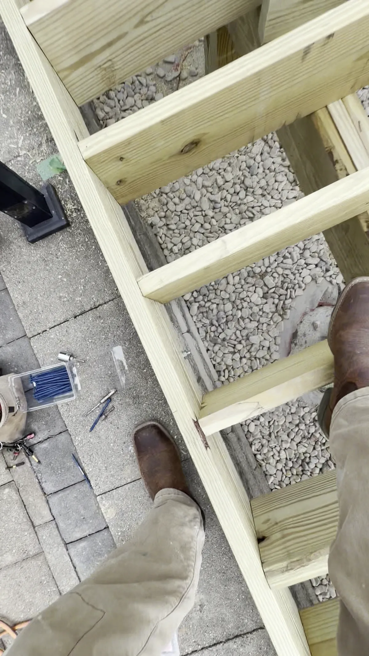 Close view of treated deck joists being fastened together over a paver surface during a deck build