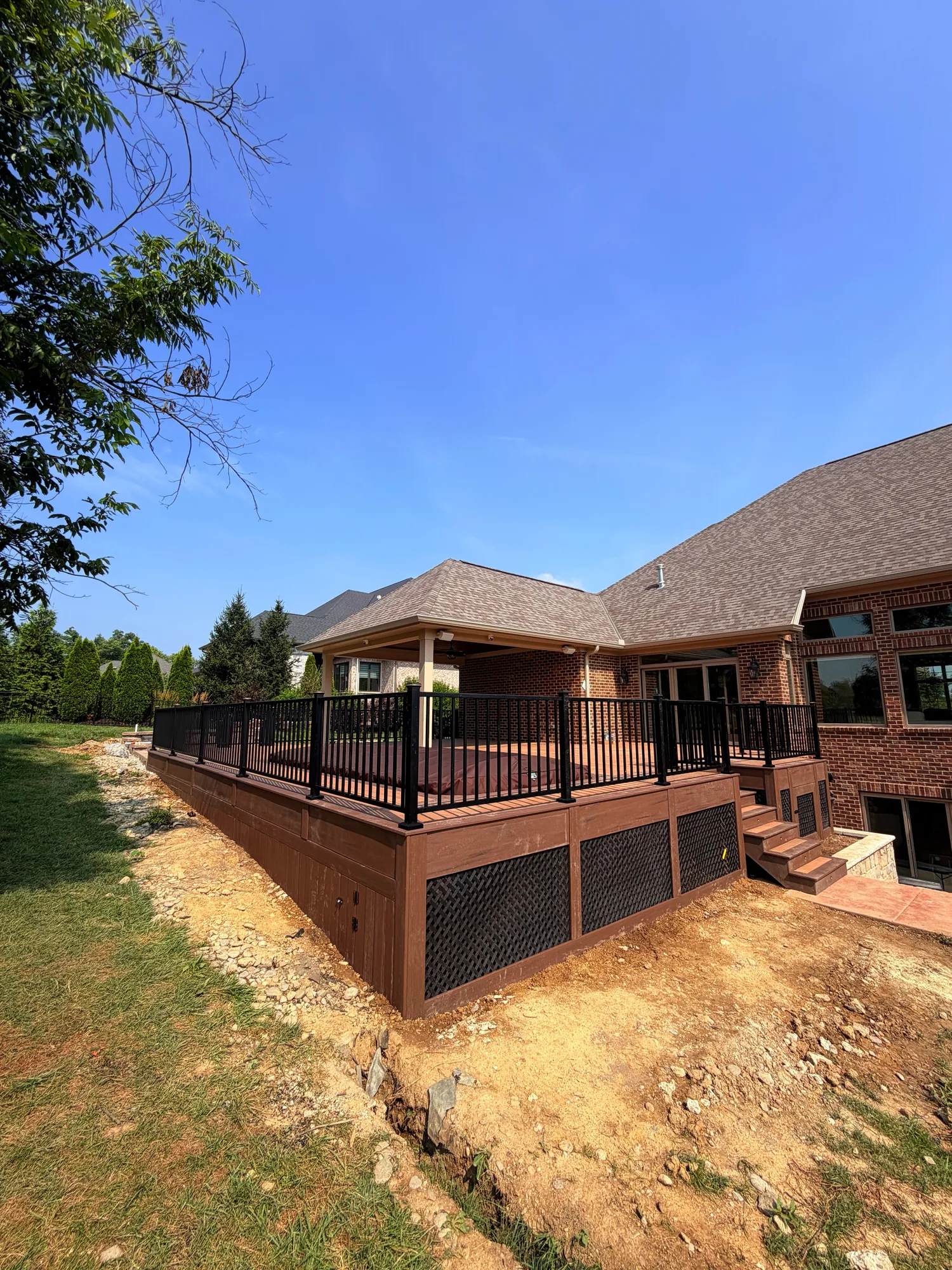 Brown composite deck with black aluminum railing across the back of a brick home above a freshly graded yard