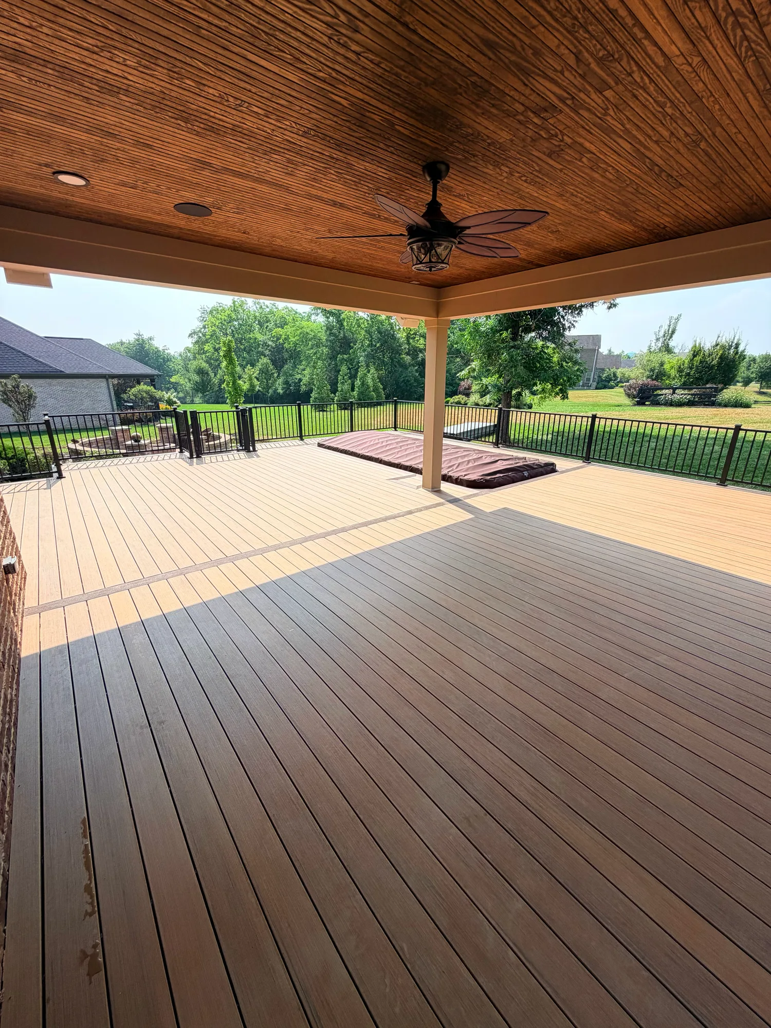 Covered outdoor space with a wood lined ceiling and ceiling fan over a brown composite deck
