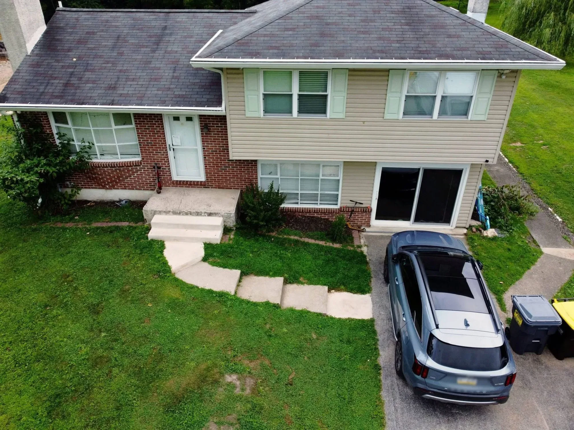 The front of a brick and siding home before the project, with plain concrete steps and an overgrown yard