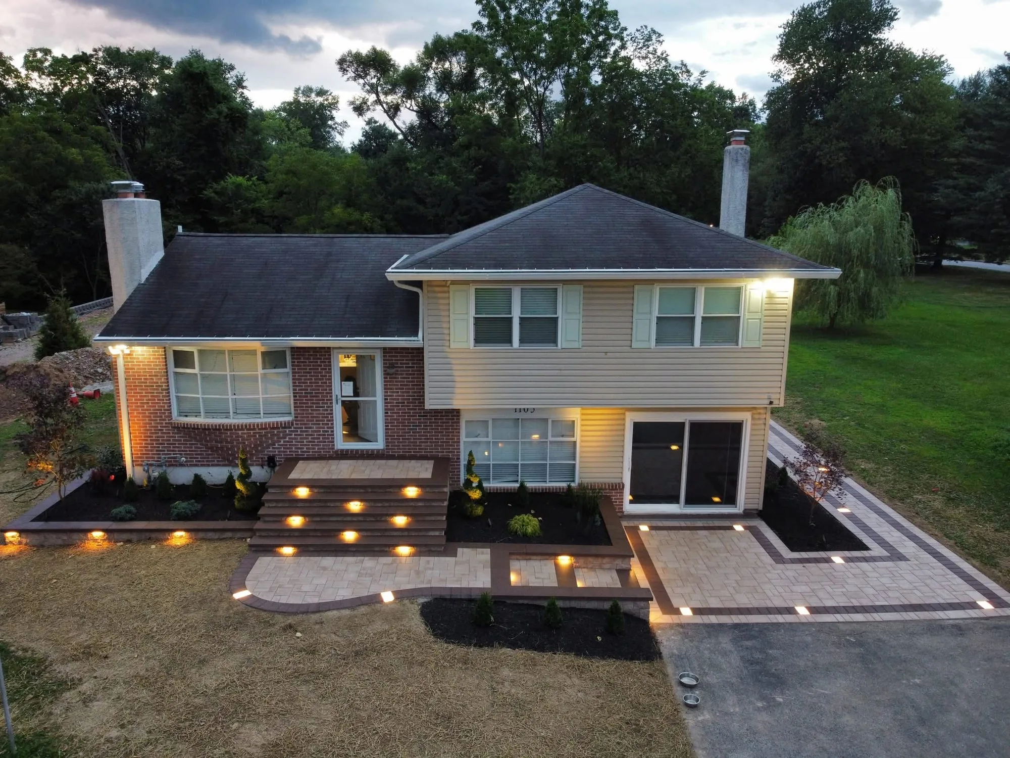 The same home after, with a paver front entrance, wide lit steps and fresh landscaping at dusk