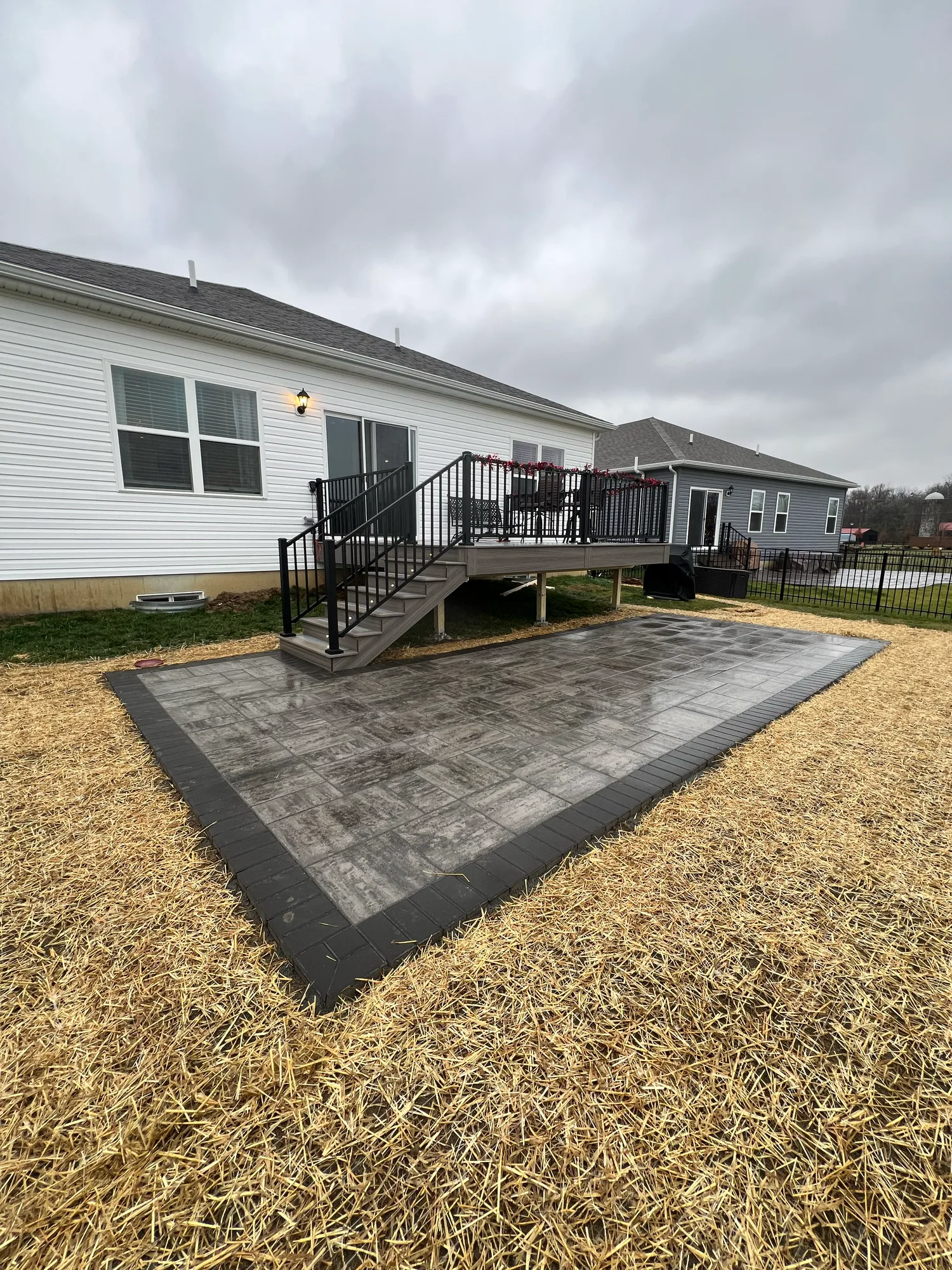 Grey composite deck with black railing above a freshly graded and strawed yard on an overcast day