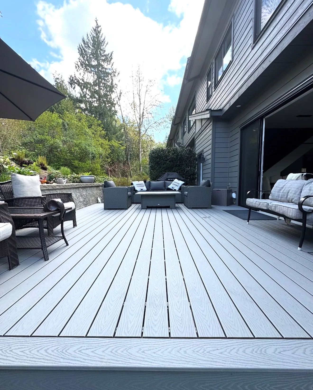 Grey composite deck with lounge seating and a fire table beside a grey sided home