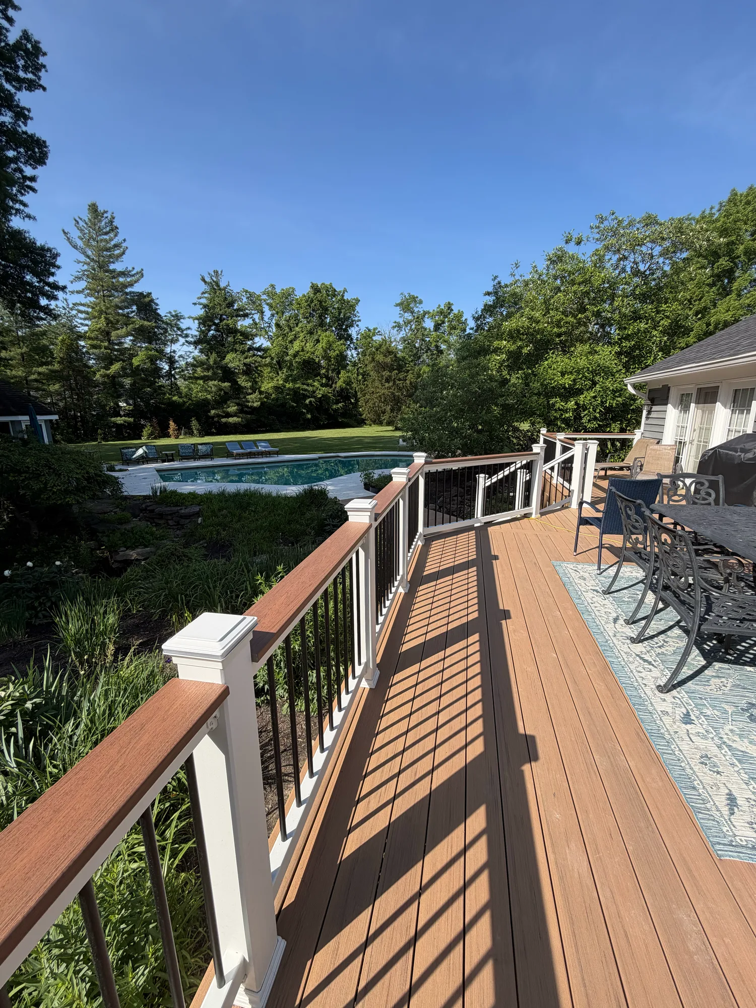 Brown composite deck with white railing overlooking a swimming pool and lawn