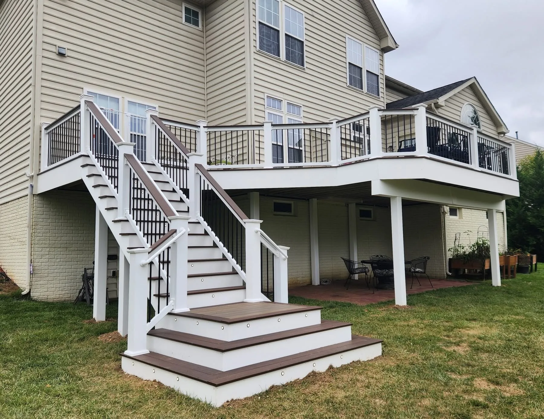 Large elevated composite deck with white railing and a double staircase down to the lawn at a tan home