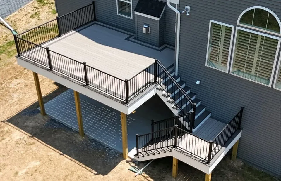 Raised composite deck with horizontal cable railing and a staircase at a grey sided home