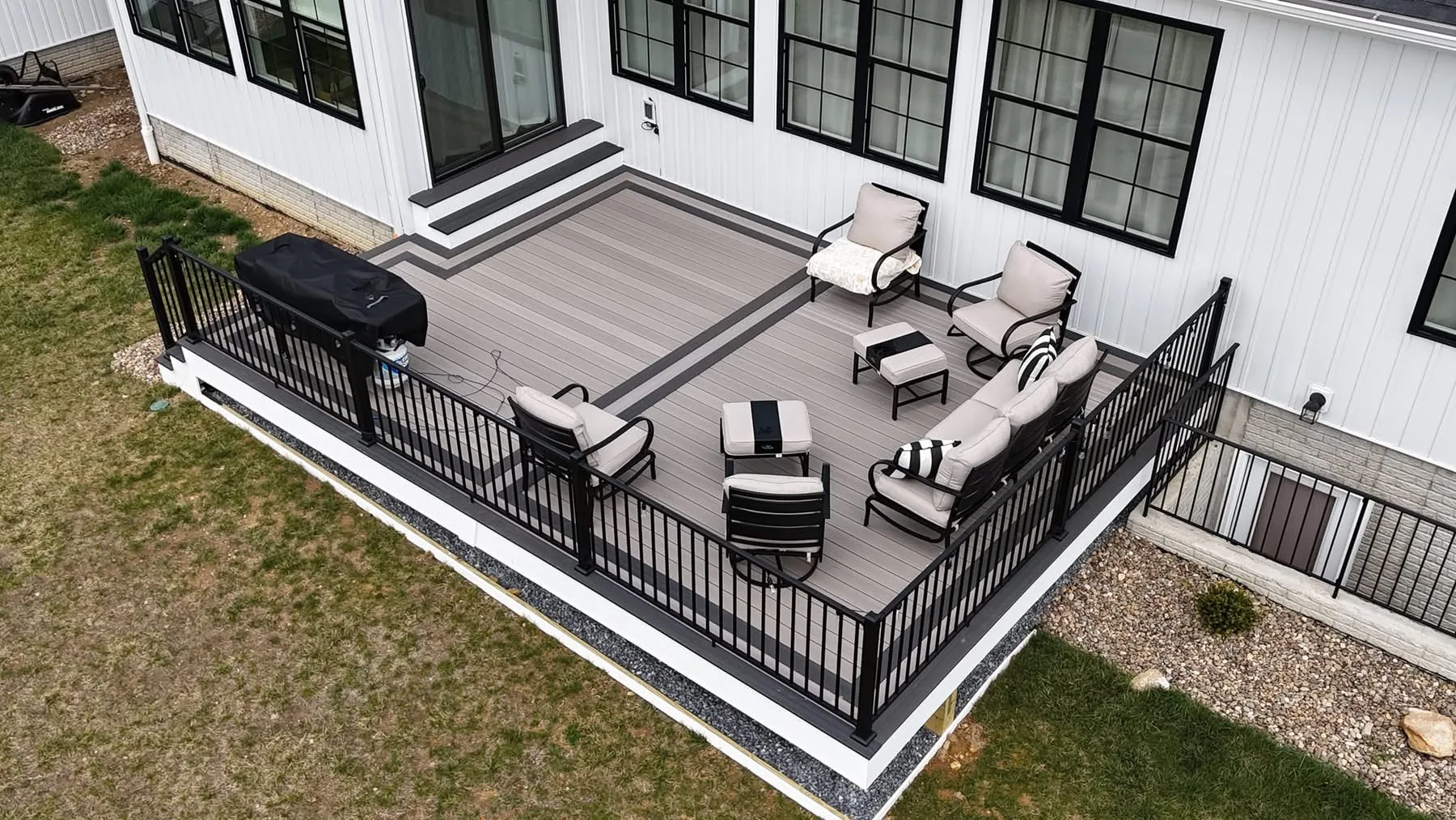 Aerial view of a grey composite deck with lounge furniture and a grill at a white home