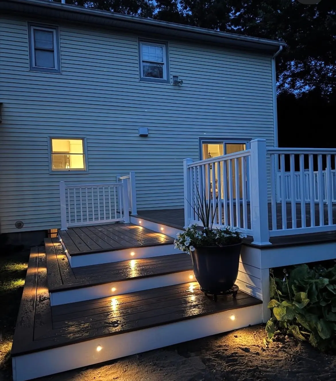 Lit composite deck steps beside white railing