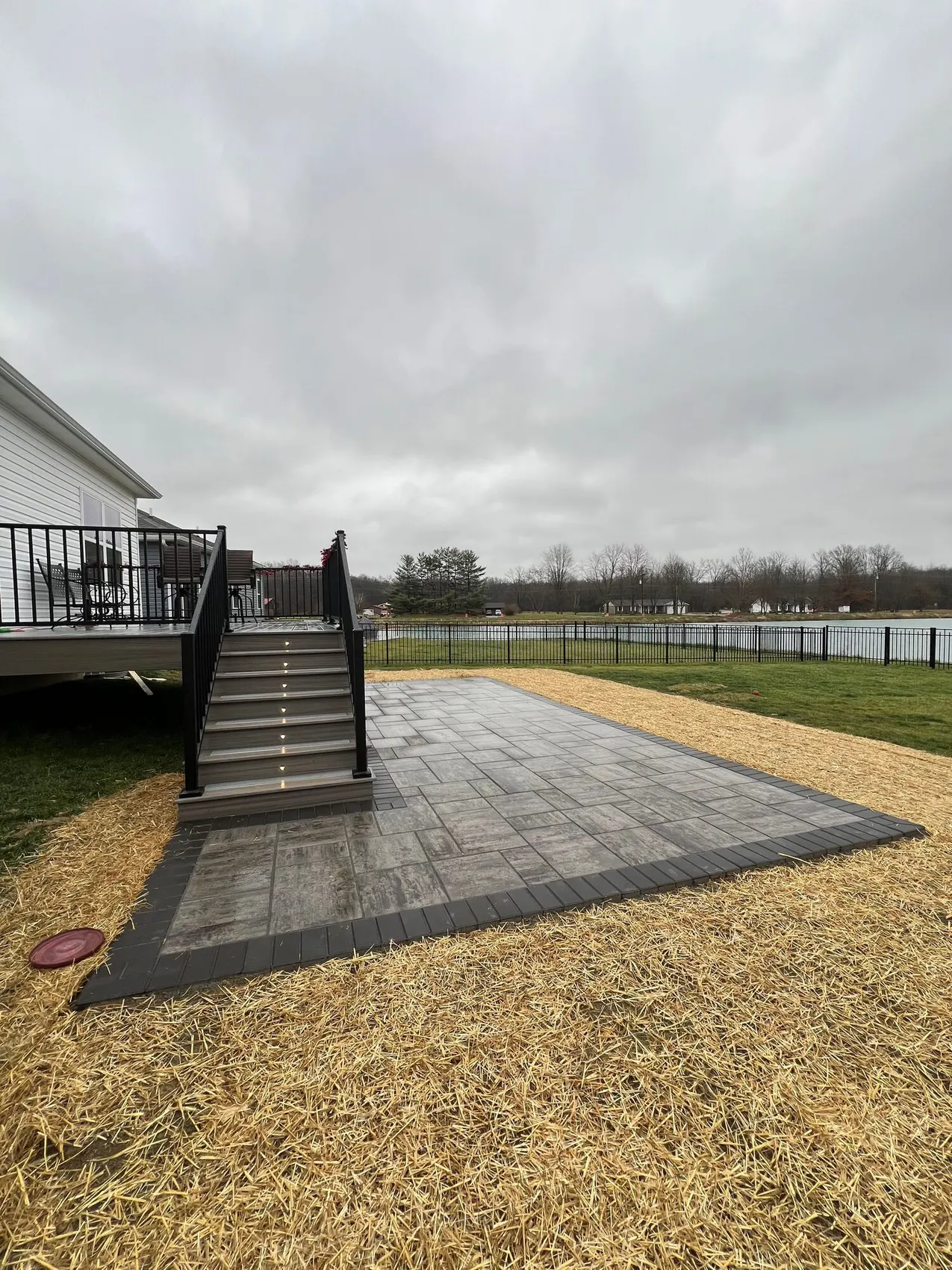 Paver patio below a deck with lit stairs leading down to it