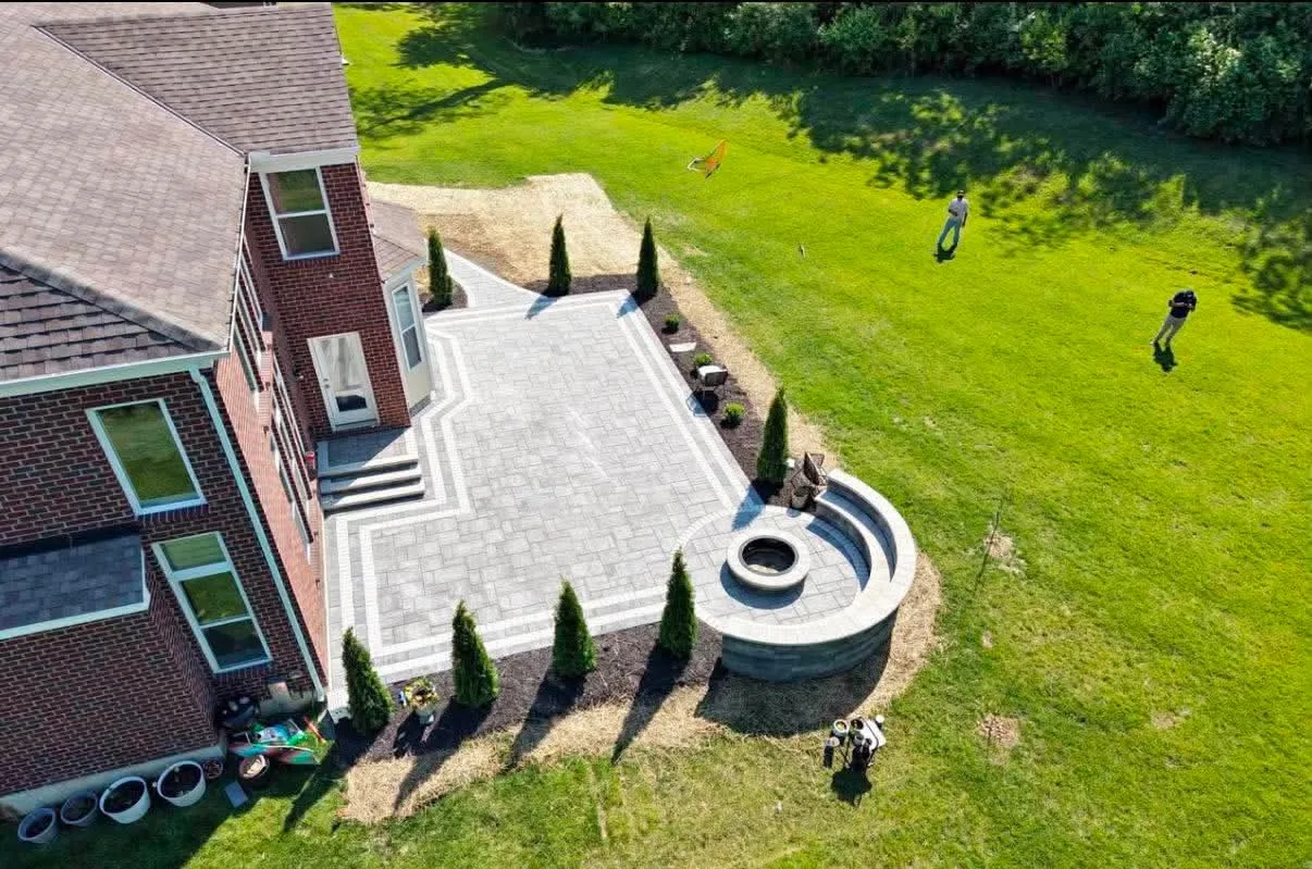 Aerial view of a grey paver patio with a round stone fire pit and curved seat wall at a brick home